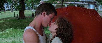 Movie still from “Mad Max” (1979), directed by George Miller – A man and a woman kissing in a park; Medium shot, Low angle
