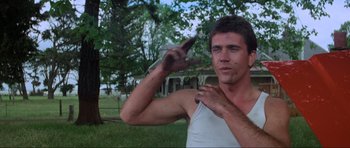 Movie still from “Mad Max” (1979), directed by George Miller – A man in a white tank top is pointing to the camera; Medium shot, Low angle