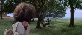 Movie still from “Mad Max” (1979), directed by George Miller – A person sitting on a bench in a field; Medium shot, Over the shoulder angle