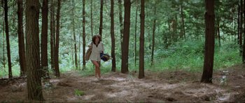 Movie still from “Mad Max” (1979), directed by George Miller – A woman walking through the woods with a backpack; Wide shot, Low angle