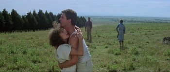 Movie still from “Mad Max” (1979), directed by George Miller – A man and a woman hugging in a field; Wide shot, Low angle
