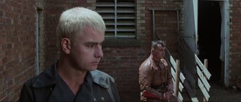 Movie still from “Mad Max” (1979), directed by George Miller – A man with white hair stands next to another man with blonde hair; Close Up shot, Low angle