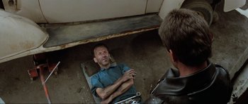 Movie still from “Mad Max” (1979), directed by George Miller – A man laying on the ground with a wrench in his hand; Medium shot, Overhead angle