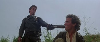 Movie still from “Mad Max” (1979), directed by George Miller – A man is holding a baseball bat over another man's face; Medium shot, Low angle