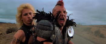 Movie still from “The Road Warrior” (1981), directed by George Miller – A man with a red mohawk is yelling at something; Close Up shot, Low angle