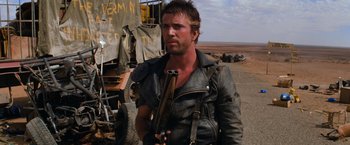 Movie still from “The Road Warrior” (1981), directed by George Miller – A man in a leather jacket holding a gun; Close Up shot, Over the shoulder angle