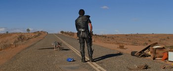 Movie still from “The Road Warrior” (1981), directed by George Miller – A man standing on the side of a road with a dog; Wide shot, Over the shoulder angle
