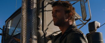 Movie still from “The Road Warrior” (1981), directed by George Miller – A person standing next to a metal fence; Close Up shot, Low angle