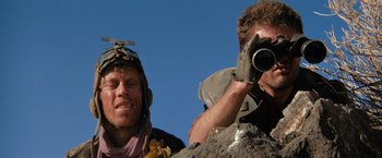 Movie still from “The Road Warrior” (1981), directed by George Miller – A man with a helmet on and a man holding a camera; Close Up shot, Low angle