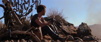 Movie still from “The Road Warrior” (1981), directed by George Miller – A man sitting on the ground in the dirt; Wide shot, Low angle
