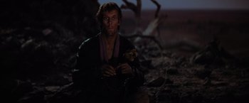 Movie still from “The Road Warrior” (1981), directed by George Miller – A man holding a skull in his hands; Medium shot, High angle