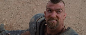 Movie still from “The Road Warrior” (1981), directed by George Miller – A person with a beard; Close Up shot, Over the shoulder angle