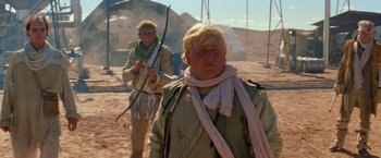 Movie still from “The Road Warrior” (1981), directed by George Miller – A man with a bow and arrow and another man with a scarf; Medium shot, Low angle