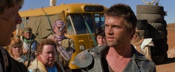 Movie still from “The Road Warrior” (1981), directed by George Miller – A group of people standing next to each other near a bus; Close Up shot, Over the shoulder angle