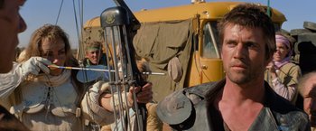 Movie still from “The Road Warrior” (1981), directed by George Miller – A group of men standing next to a yellow truck; Close Up shot, Over the shoulder angle