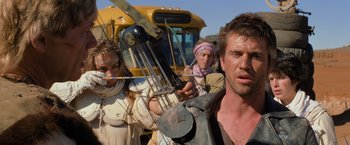 Movie still from “The Road Warrior” (1981), directed by George Miller – A group of people standing next to each other near a bus; Medium shot, Low angle