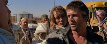 Movie still from “The Road Warrior” (1981), directed by George Miller – A group of people standing next to each other on top of a field; Close Up shot, Over the shoulder angle