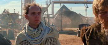 Movie still from “The Road Warrior” (1981), directed by George Miller – A man wearing a scarf standing in the dirt; Close Up shot, Low angle