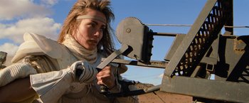 Movie still from “The Road Warrior” (1981), directed by George Miller – A woman in a costume working on an object; Close Up shot, Low angle