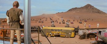 Movie still from “The Road Warrior” (1981), directed by George Miller – A yellow school bus parked in the middle of the desert; Extreme Wide shot, High angle