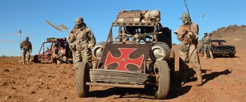 Movie still from “The Road Warrior” (1981), directed by George Miller – An old car with an iron cross on the front; Wide shot, Low angle