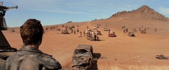 Movie still from “The Road Warrior” (1981), directed by George Miller – A group of people standing next to cars on a dirt road; Extreme Wide shot, High angle