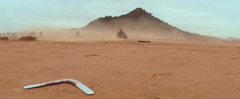 Movie still from “The Road Warrior” (1981), directed by George Miller – A dirt field with a truck in the background; Extreme Wide shot, Low angle