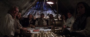 Movie still from “The Road Warrior” (1981), directed by George Miller – A group of people sitting at a table in front of an eiffel tower; Wide shot, Low angle