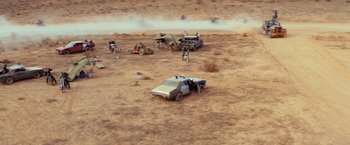 Movie still from “The Road Warrior” (1981), directed by George Miller – A group of people standing next to cars in the desert; Extreme Wide shot, High angle