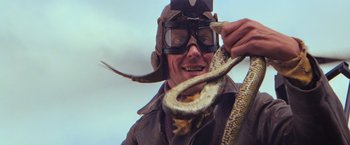 Movie still from “The Road Warrior” (1981), directed by George Miller – An old man wearing a hat and goggles holding a snake; Close Up shot, Low angle