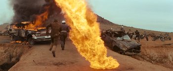 Movie still from “The Road Warrior” (1981), directed by George Miller – Two men running away from a fire in the desert; Wide shot, Low angle