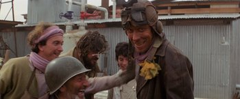 Movie still from “The Road Warrior” (1981), directed by George Miller – A group of people in a field with a person wearing a helmet; Close Up shot, Over the shoulder angle
