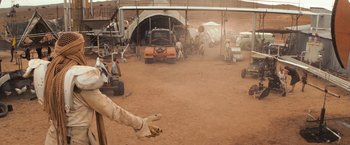 Movie still from “The Road Warrior” (1981), directed by George Miller – A group of people working on a car in a dirt field; Wide shot, High angle