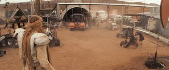 Movie still from “The Road Warrior” (1981), directed by George Miller – A dirt field with a lot of vehicles parked in it; Wide shot, Over the shoulder angle