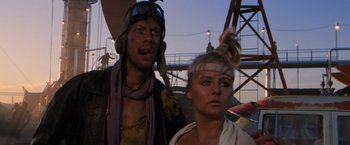 Movie still from “The Road Warrior” (1981), directed by George Miller – A man and a woman standing next to each other under an umbrella; Close Up shot, Low angle