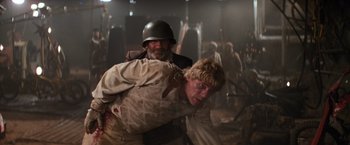 Movie still from “The Road Warrior” (1981), directed by George Miller – A man in a helmet is wrestling a man in a uniform; Medium shot, Over the shoulder angle