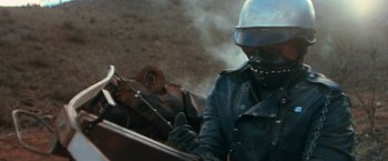 Movie still from “The Road Warrior” (1981), directed by George Miller – A man in a helmet is standing next to a horse; Close Up shot, Over the shoulder angle