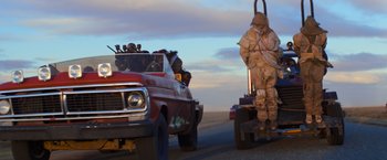 Movie still from “The Road Warrior” (1981), directed by George Miller – A truck driving down a street next to a trailer; Wide shot, Low angle