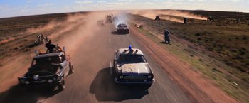 Movie still from “The Road Warrior” (1981), directed by George Miller – A group of cars driving down a dusty road; Extreme Wide shot, High angle