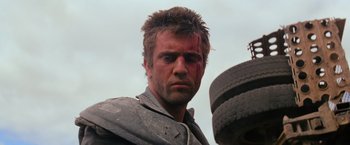 Movie still from “The Road Warrior” (1981), directed by George Miller – A person with a bandage on his face; Close Up shot, Low angle