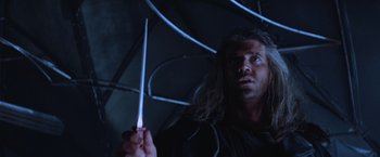 Movie still from “Mad Max Beyond Thunderdome” (1985), directed by George Miller – A man with long hair holding a knife in a dark room; Close Up shot, Low angle