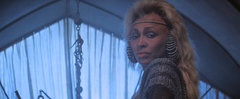 Movie still from “Mad Max Beyond Thunderdome” (1985), directed by George Miller – A woman in a silver outfit with a chain around her neck; Close Up shot, Over the shoulder angle