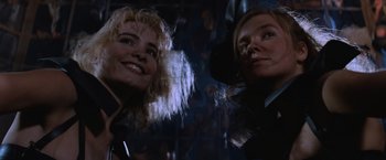 Movie still from “Mad Max Beyond Thunderdome” (1985), directed by George Miller – Two women smiling for the camera in a dark room; Close Up shot, Low angle