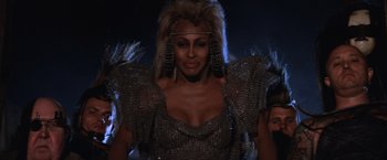 Movie still from “Mad Max Beyond Thunderdome” (1985), directed by George Miller – A woman in a silver dress and a silver wig; Medium shot, Low angle