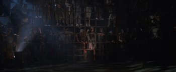 Movie still from “Mad Max Beyond Thunderdome” (1985), directed by George Miller – A group of people standing in front of a cage; Wide shot, High angle