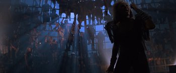 Movie still from “Mad Max Beyond Thunderdome” (1985), directed by George Miller – A woman in a black dress is standing in front of a window; Wide shot, Low angle