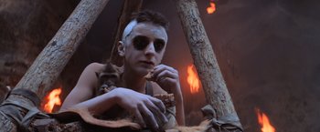 Movie still from “Mad Max Beyond Thunderdome” (1985), directed by George Miller – A man eating a piece of food while wearing makeup; Close Up shot, Low angle