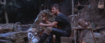 Movie still from “Mad Max Beyond Thunderdome” (1985), directed by George Miller – A man kneeling down on a rock with a stick; Medium shot, Low angle