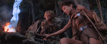 Movie still from “Mad Max Beyond Thunderdome” (1985), directed by George Miller – A woman and a boy sitting next to each other on rocks; Medium shot, Low angle