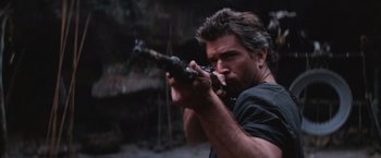 Movie still from “Mad Max Beyond Thunderdome” (1985), directed by George Miller – A man is holding a gun in his hands; Close Up shot, Over the shoulder angle